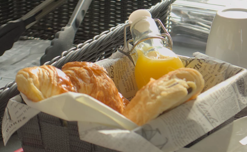 Photo d'un panier contenant le petit déjeuner continental, dans le panier il y à un jus d'orange en bouteille, un croissant et un pain au chocolat